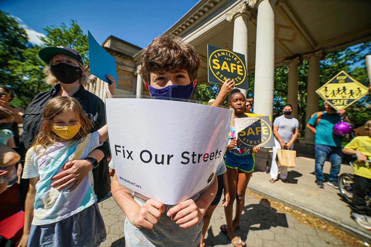 child holding sign that says "fix our streets" at mcguinness boulevard