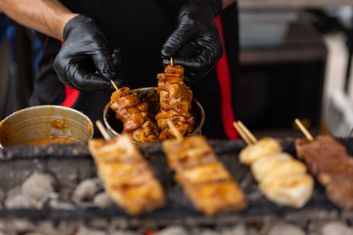 person cooking meat kebabs at smorgasburg